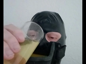 Gay BDSM scene with a latex-covered submissive who is made to drink pee from a cock ring gag.