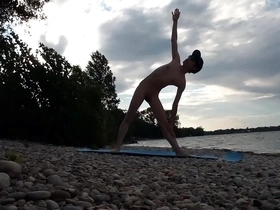 A slender nudist young man performs yoga at a naturist beach.