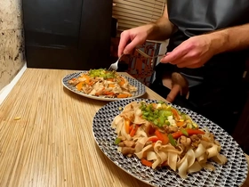 A naked gay chef cooks rice noodles with chicken and vegetables.